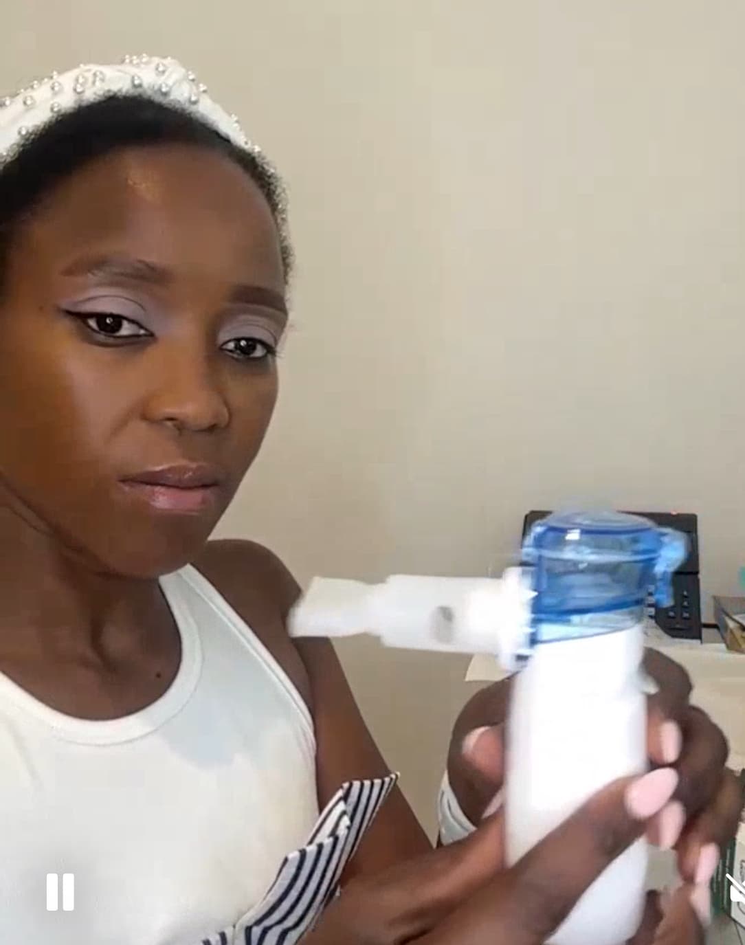 Black woman with a white headband holds a white and blue portable nebulizer medical device.